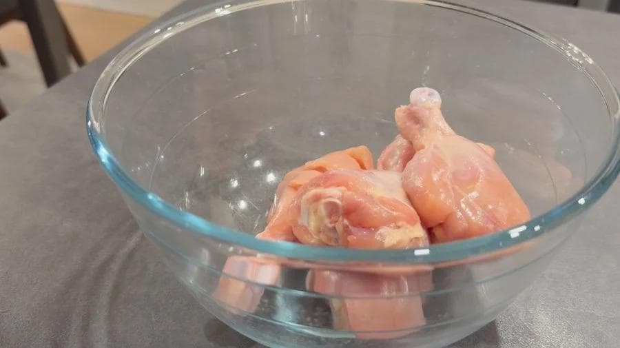 Raw chicken drumsticks marinating in a glass bowl with lemon juice and spices for tandoori chicken.
