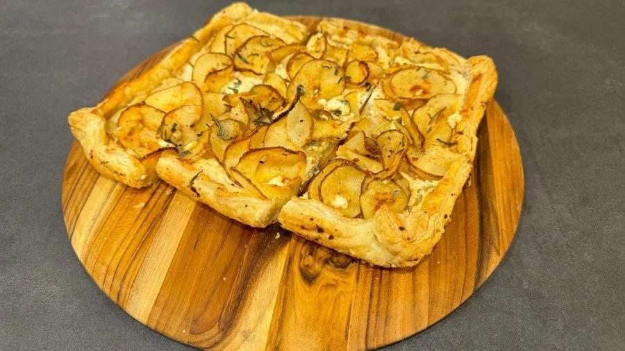 Golden puff pastry tarts topped with thinly sliced roasted potatoes on a wooden board.