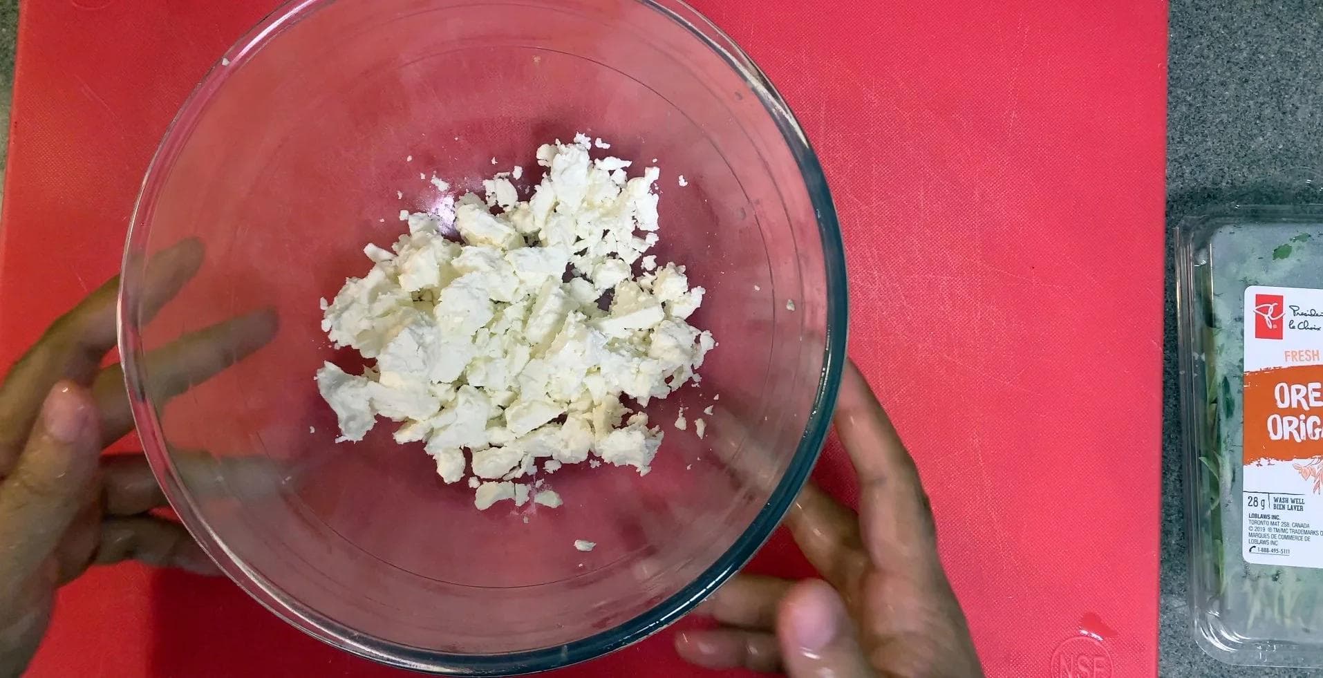 Crumbled feta cheese mixed with oregano leaves, salt, olive oil, and lemon zest in a glass bowl.