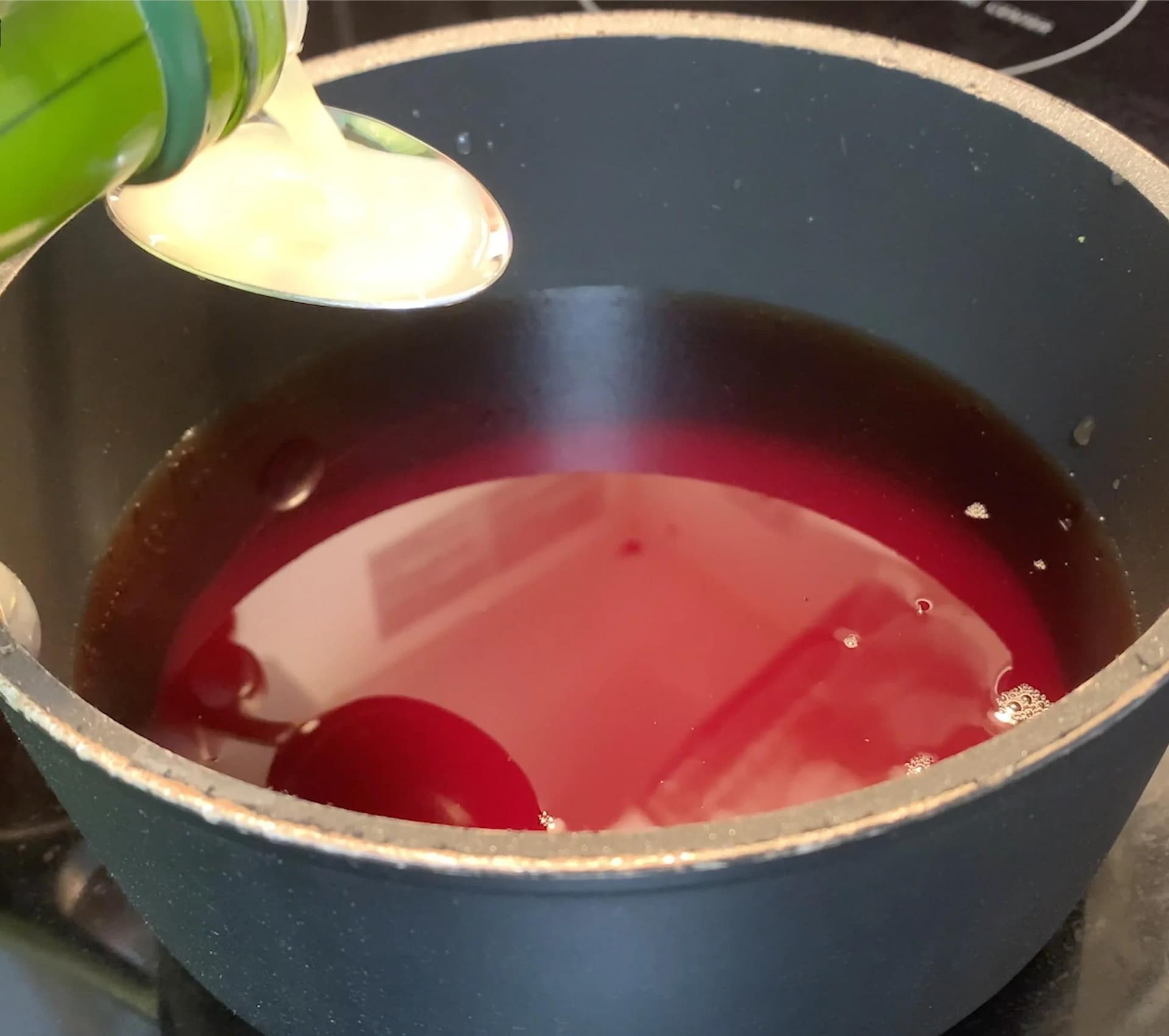 Pomegranate juice reducing in a dark pot with a light-colored spoon stirring the deep red liquid.