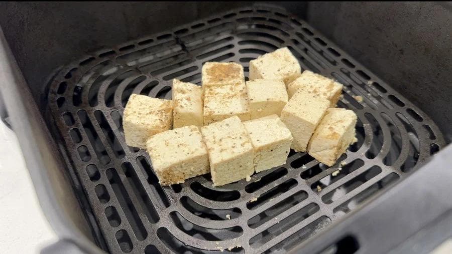 Cubed tofu pieces arranged with space between them in an air fryer basket.