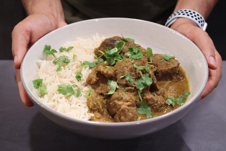 Balinese beef rendang served in a white bowl with white rice and garnished with fresh cilantro.