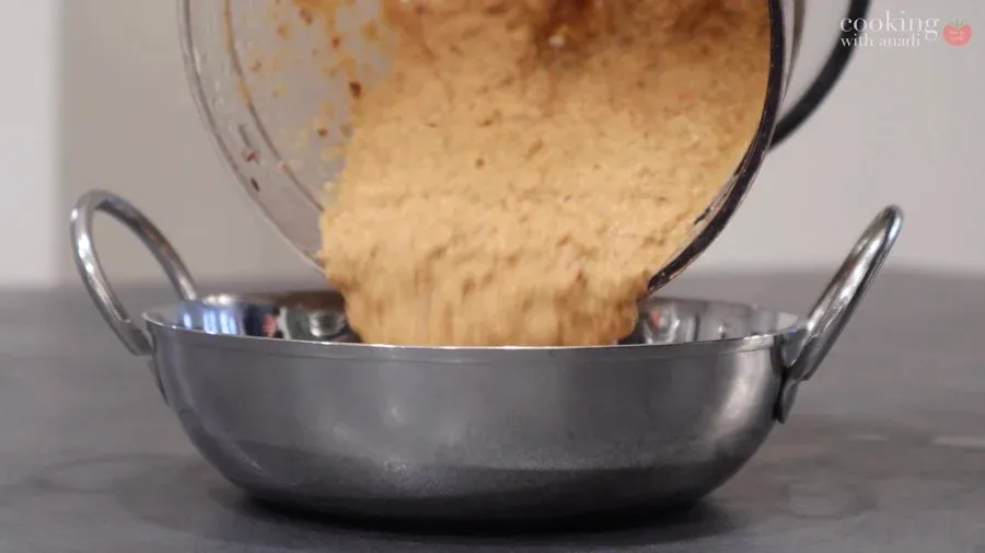 Smooth peanut chutney being poured from a blender into a dark metal bowl.