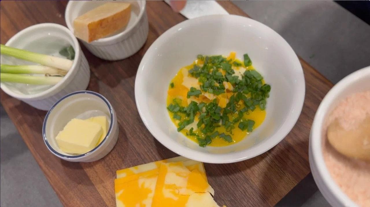 Egg yolk mixture with chopped green onions and shredded cheese in a white bowl, surrounded by prep ingredients.