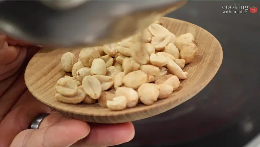 Roasted cashews in a wooden spoon held in hand during tofu noodle stir fry preparation.