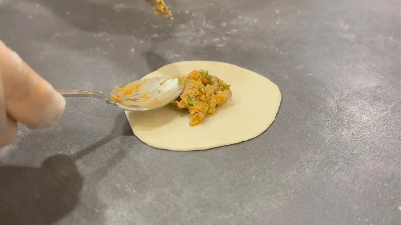 Sealed momo dumpling with pleated edges on a white plate, held with a fork during preparation.
