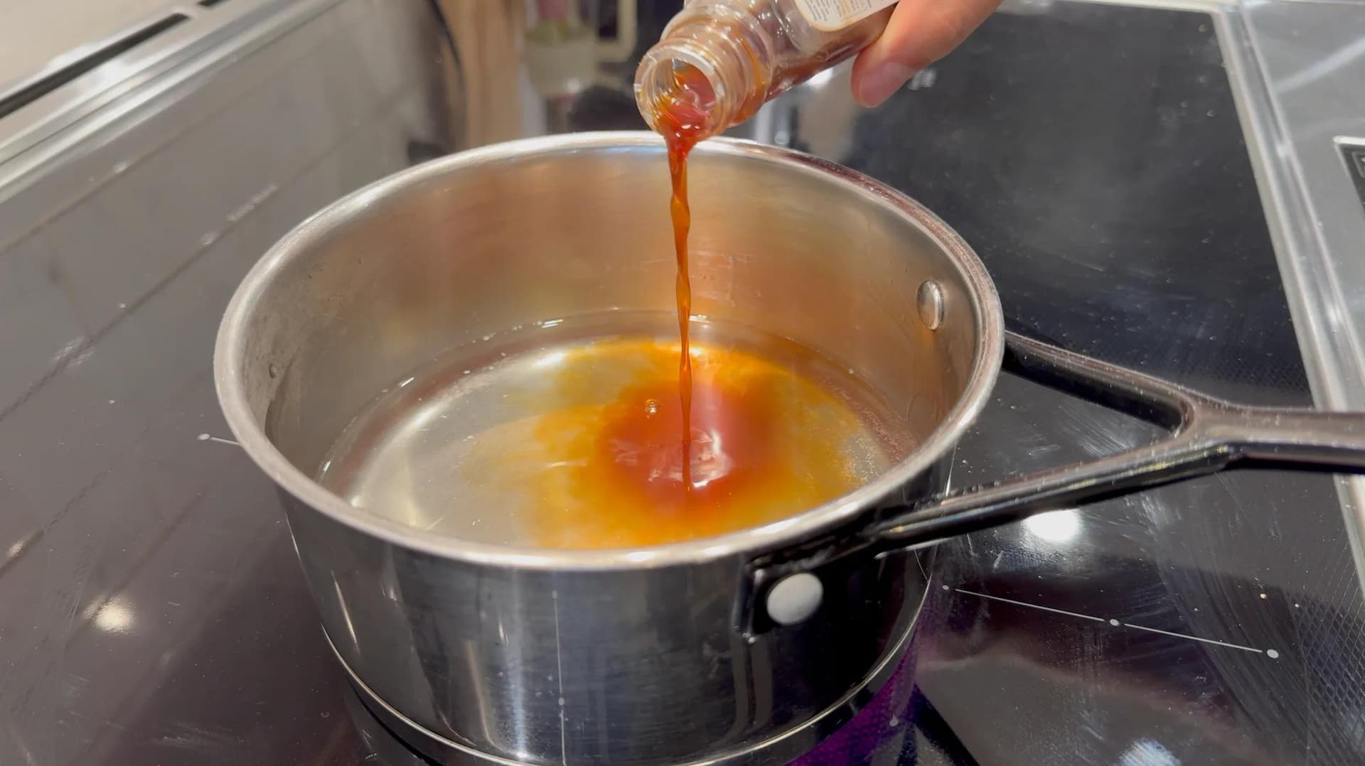 Vanilla extract being poured into a saucepan of dissolved sugar and water on a stovetop.