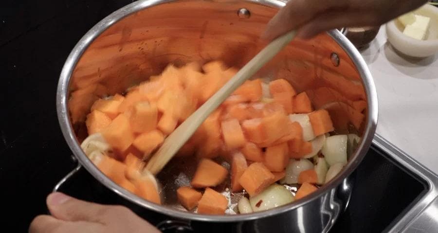 Wooden spoon stirring diced carrots and onions in a pot of simmering liquid.