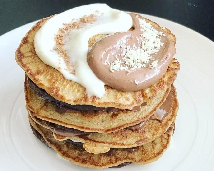 Stack of four cinnamon pancakes topped with chocolate and vanilla cream cheese frosting and crushed cookies.