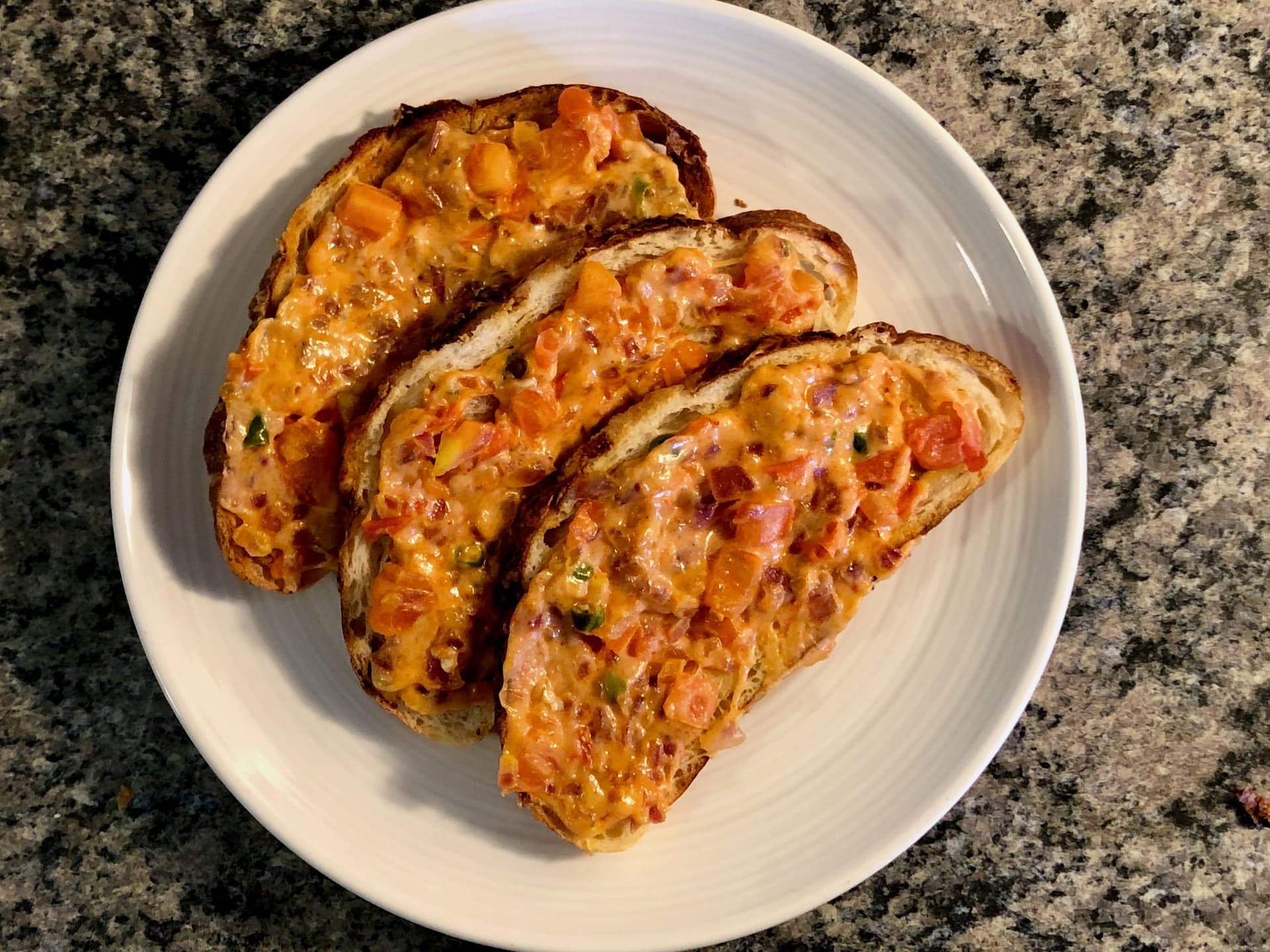 Three slices of Indian masala cheese toast with melted cheese and spices on a white plate.