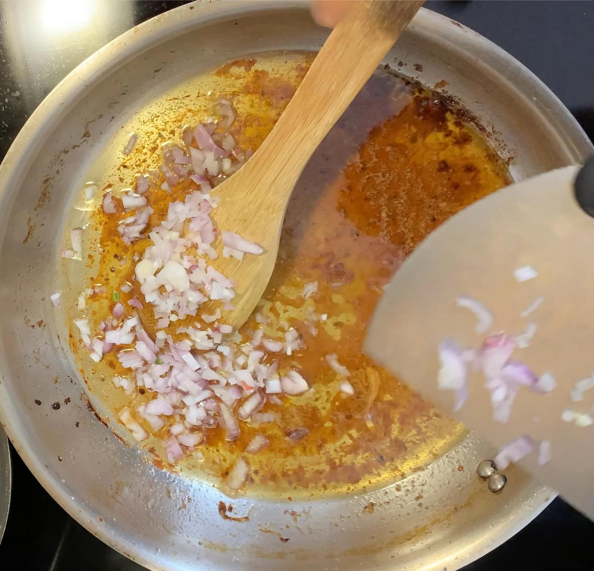 Shallots being stirred into a pan of golden pan drippings and fond with a wooden spoon.