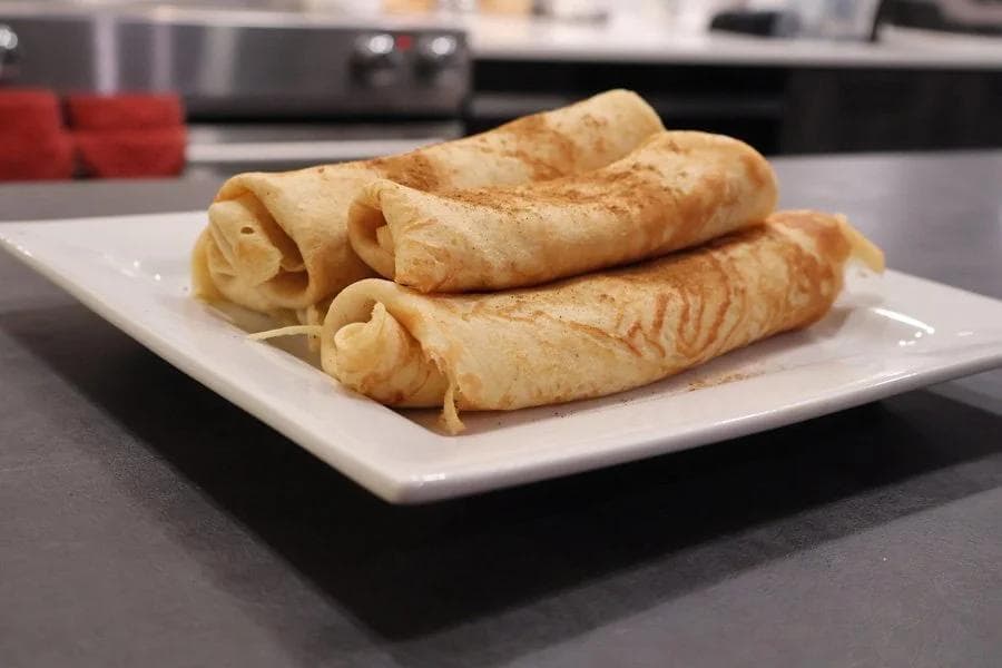 Rolled pumpkin crepes stacked on a white plate, dusted with cinnamon.