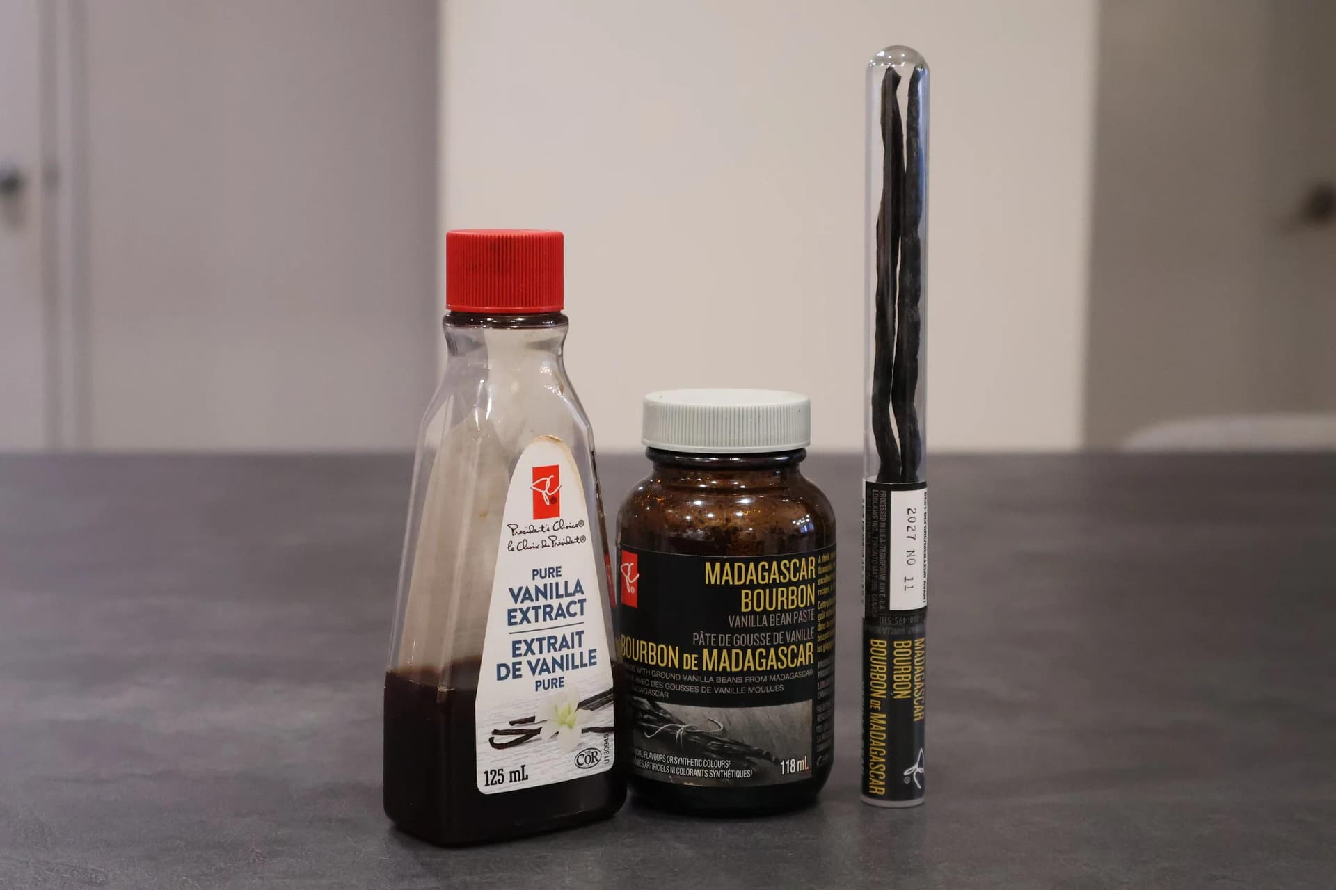 Three vanilla extract bottles displayed on a gray surface for homemade vanilla syrup recipe ingredients.