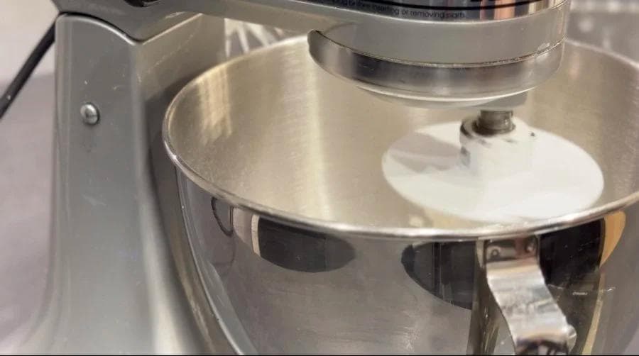Stand mixer with dough hook mixing beavertail dough in stainless steel bowl.
