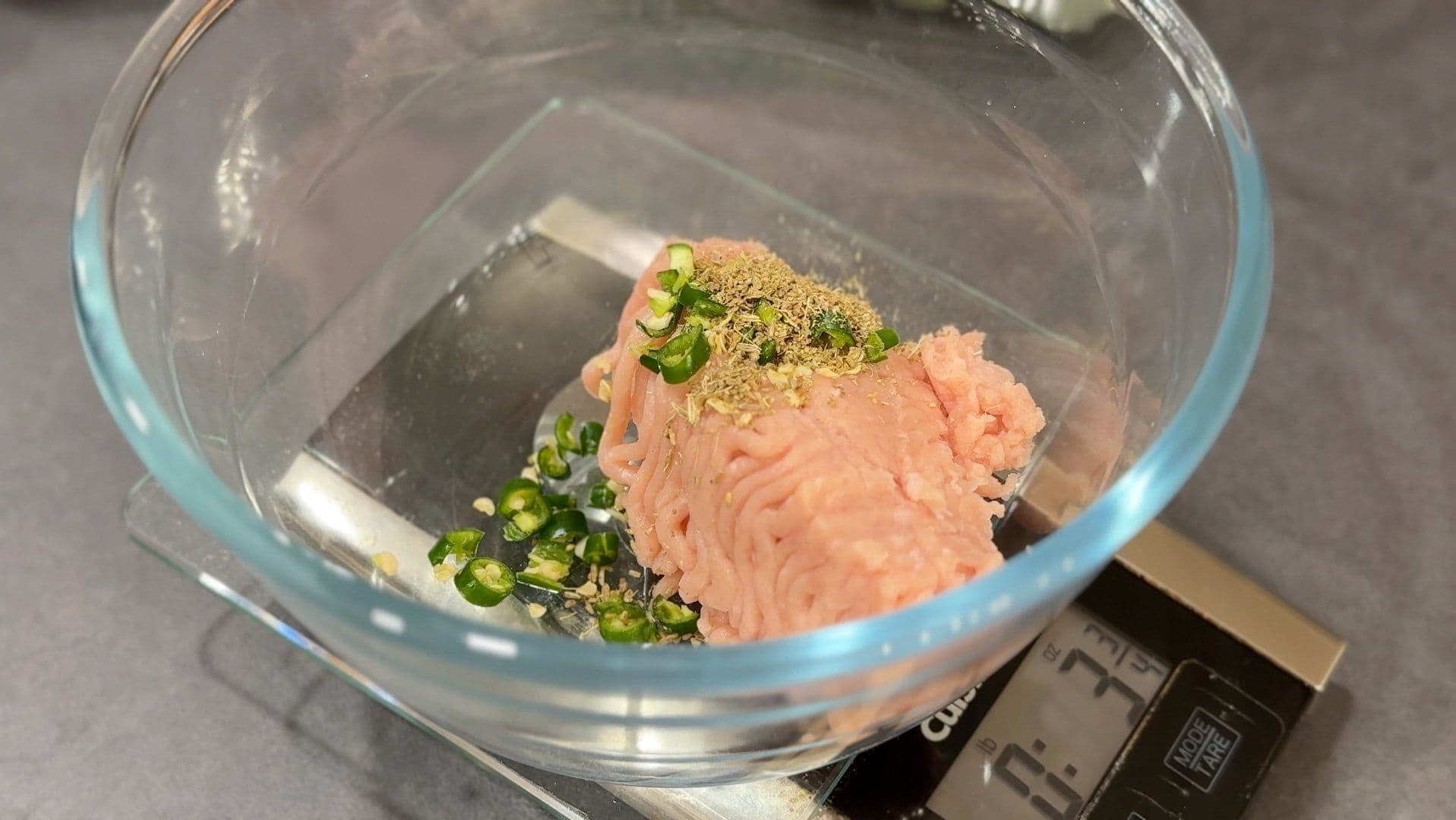 Ground meat mixed with green peppers and spices in a glass bowl on a kitchen scale.