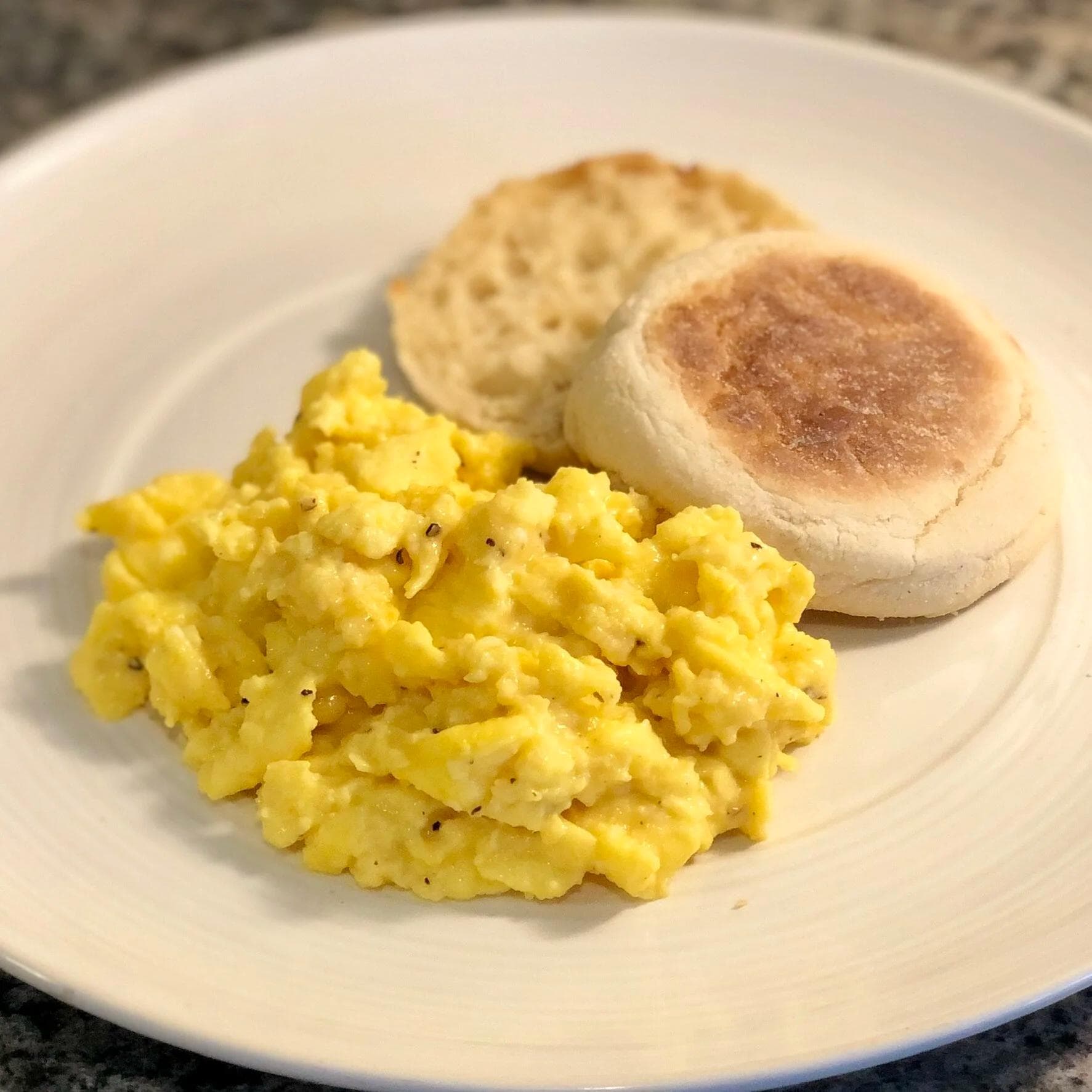 Fluffy scrambled eggs with black pepper served on a plate with buttered English muffin and toast.