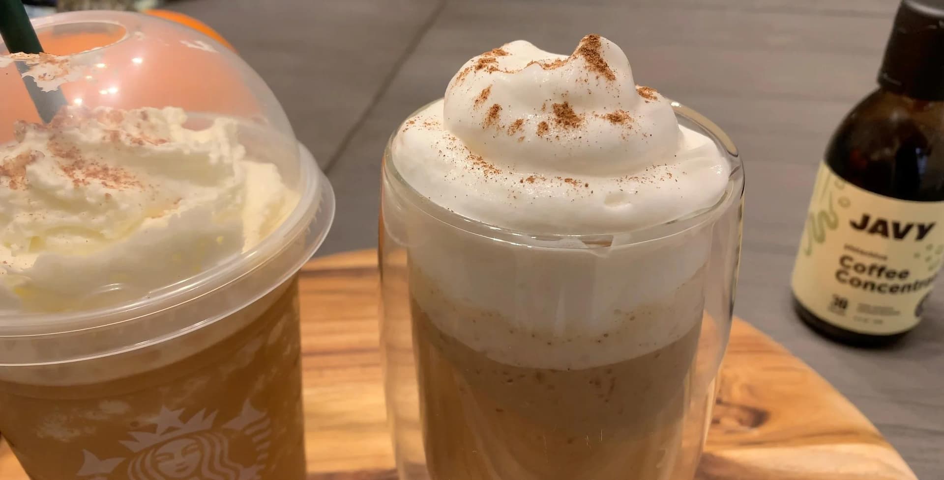 Two pumpkin spice frappuccinos topped with whipped cream and cinnamon, with a coffee concentrate bottle nearby.