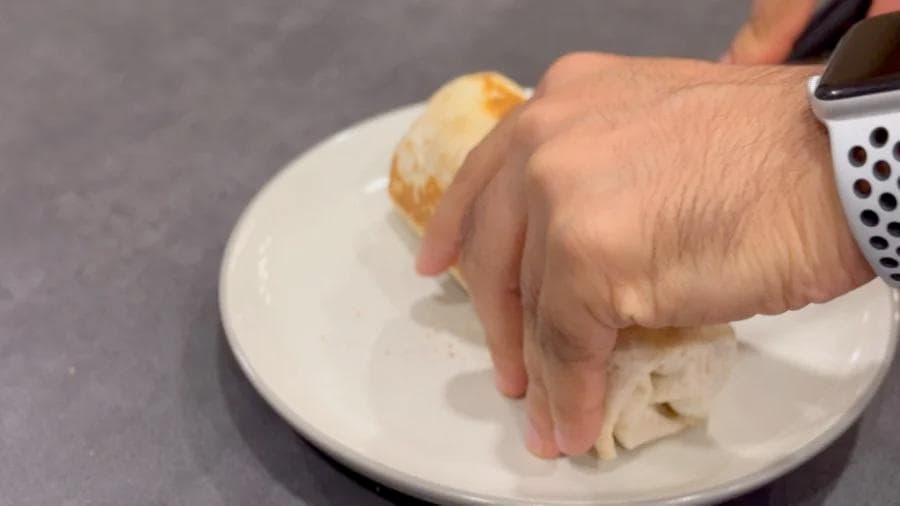 Hand grating white cheese onto a plate with a toasted burrito and bread roll.