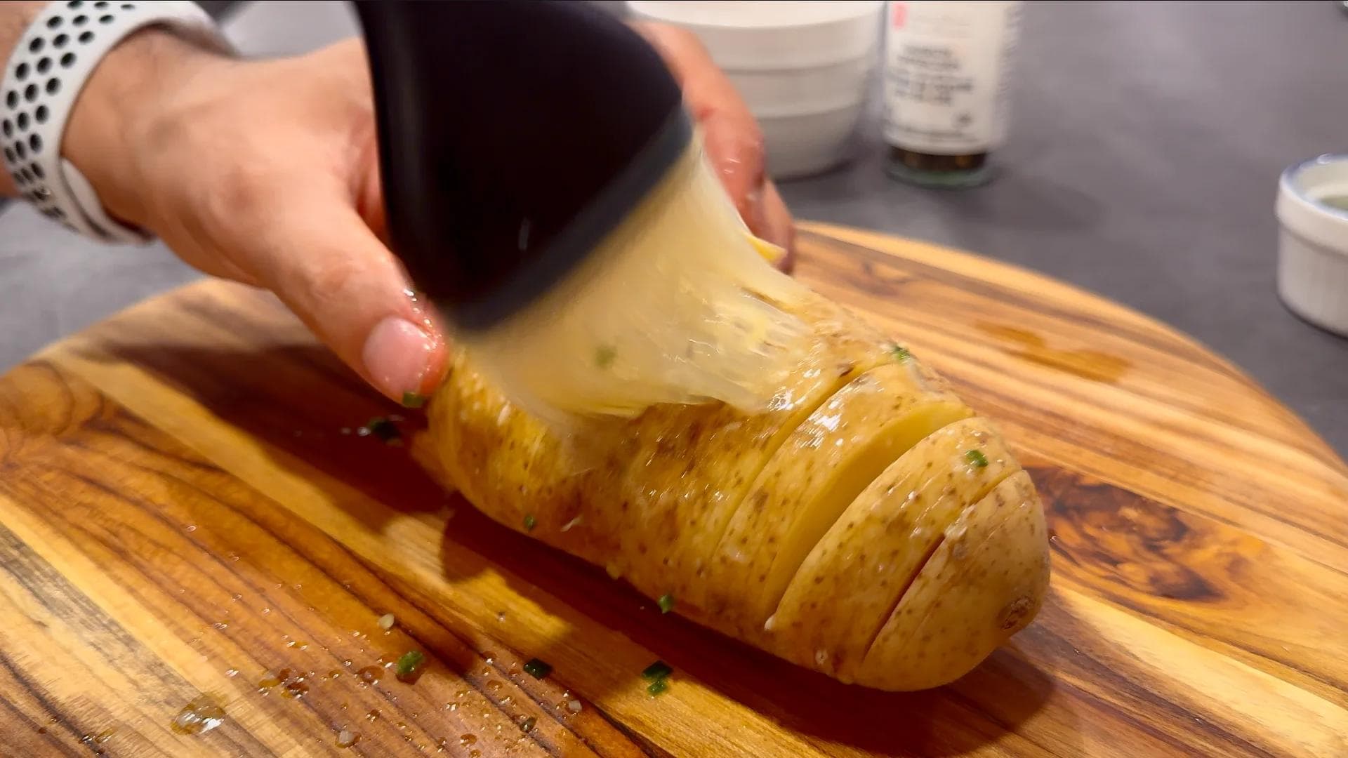 Brushing olive oil onto sliced hasselback potato on wooden cutting board