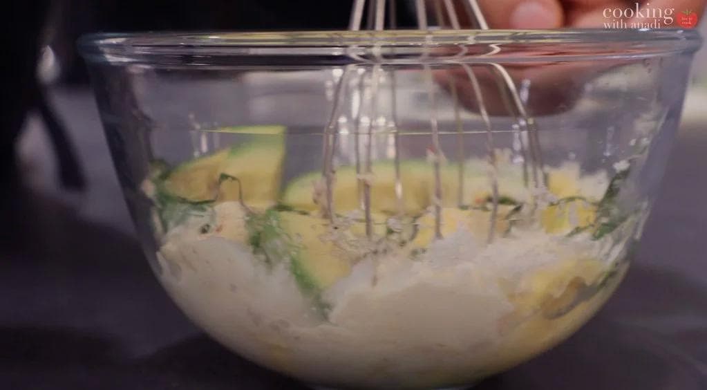 Whisking deviled egg mixture with avocado and green chilies in a glass bowl until smooth.