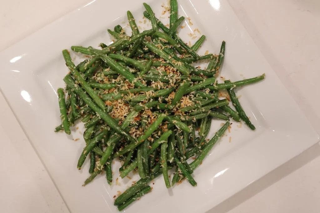 Sautéed green beans with toasted coconut and garlic served on a white plate
