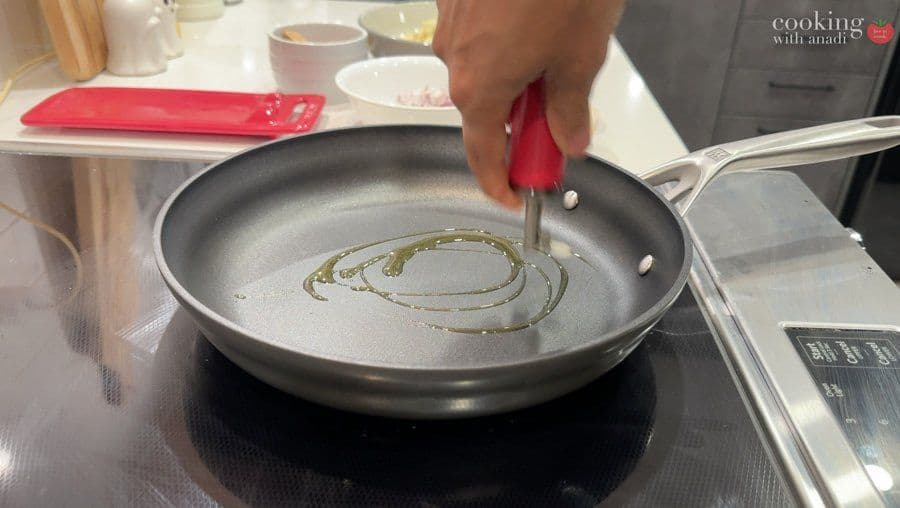 Oil swirling in a skillet with cumin seeds and spices being heated on medium flame for aloo patty filling.