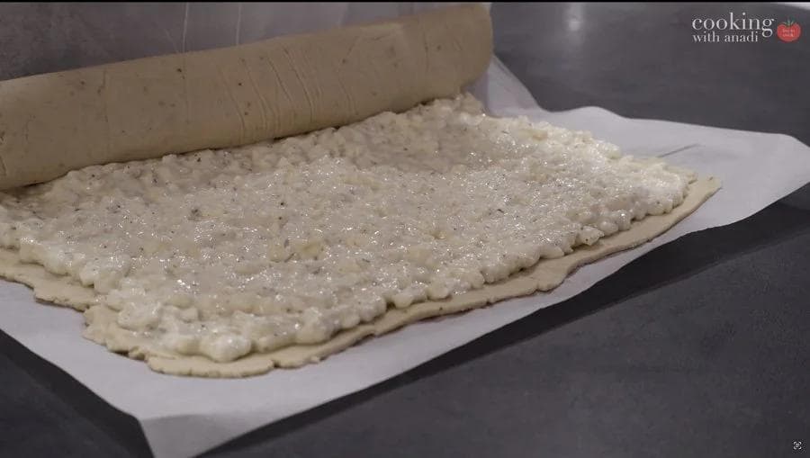 Gluten-free dough spread with cheese filling on parchment paper, ready to be rolled into a log.