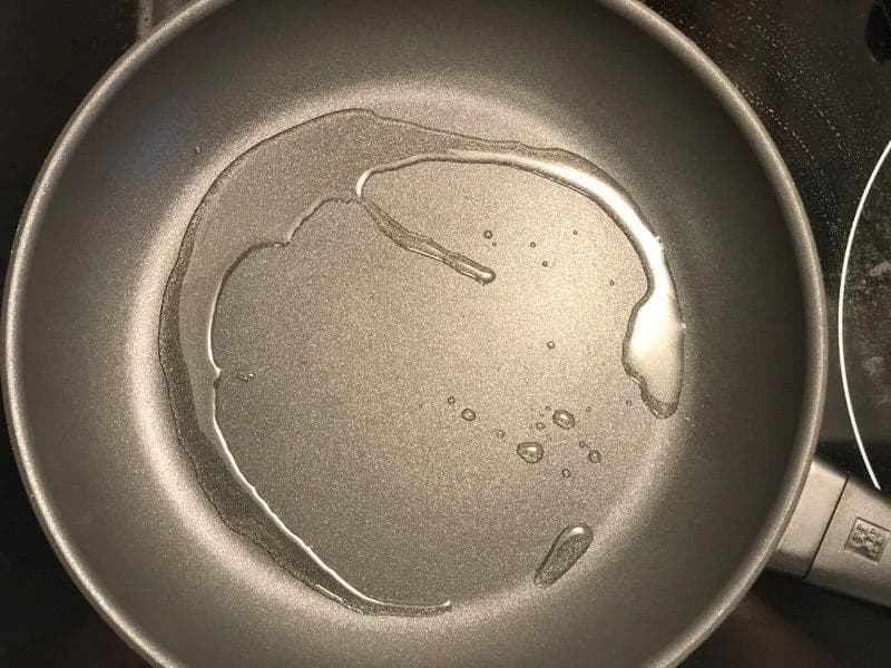 Cumin seeds crackling in hot oil in a stainless steel pan on medium heat.