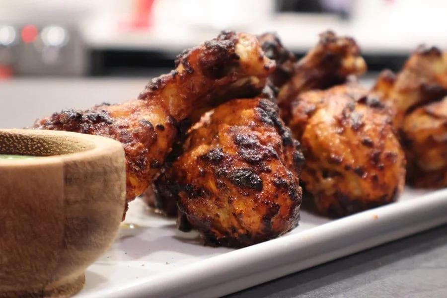 Air fryer tandoori chicken pieces with charred, golden-brown exterior served on white plate with dipping sauce.