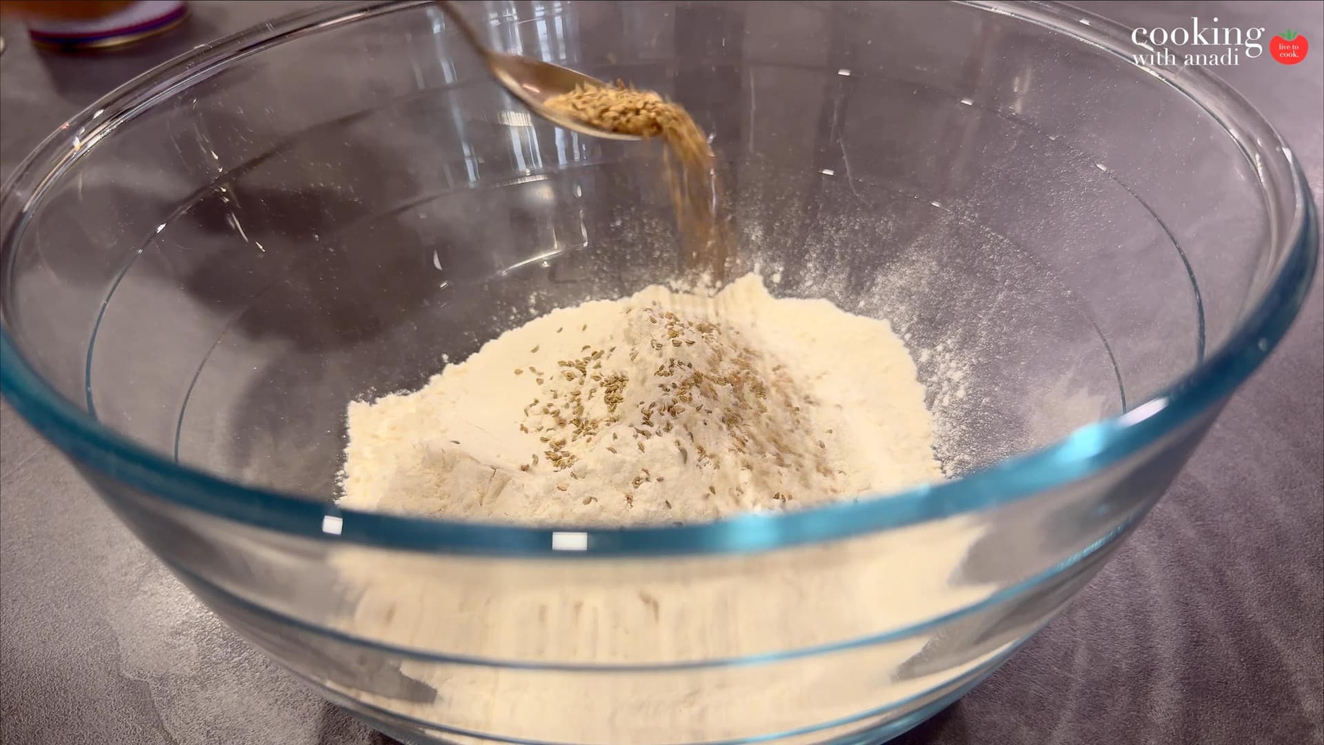 Flour mixed with ajwain seeds and ghee in a glass bowl with crumbly texture during samosa dough preparation.