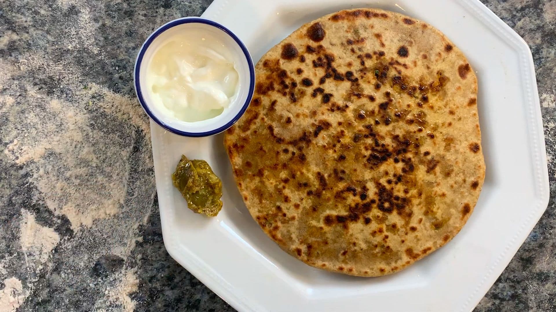 Stuffed chicken keema paratha served on a white plate with yogurt and pickled mango on the side.