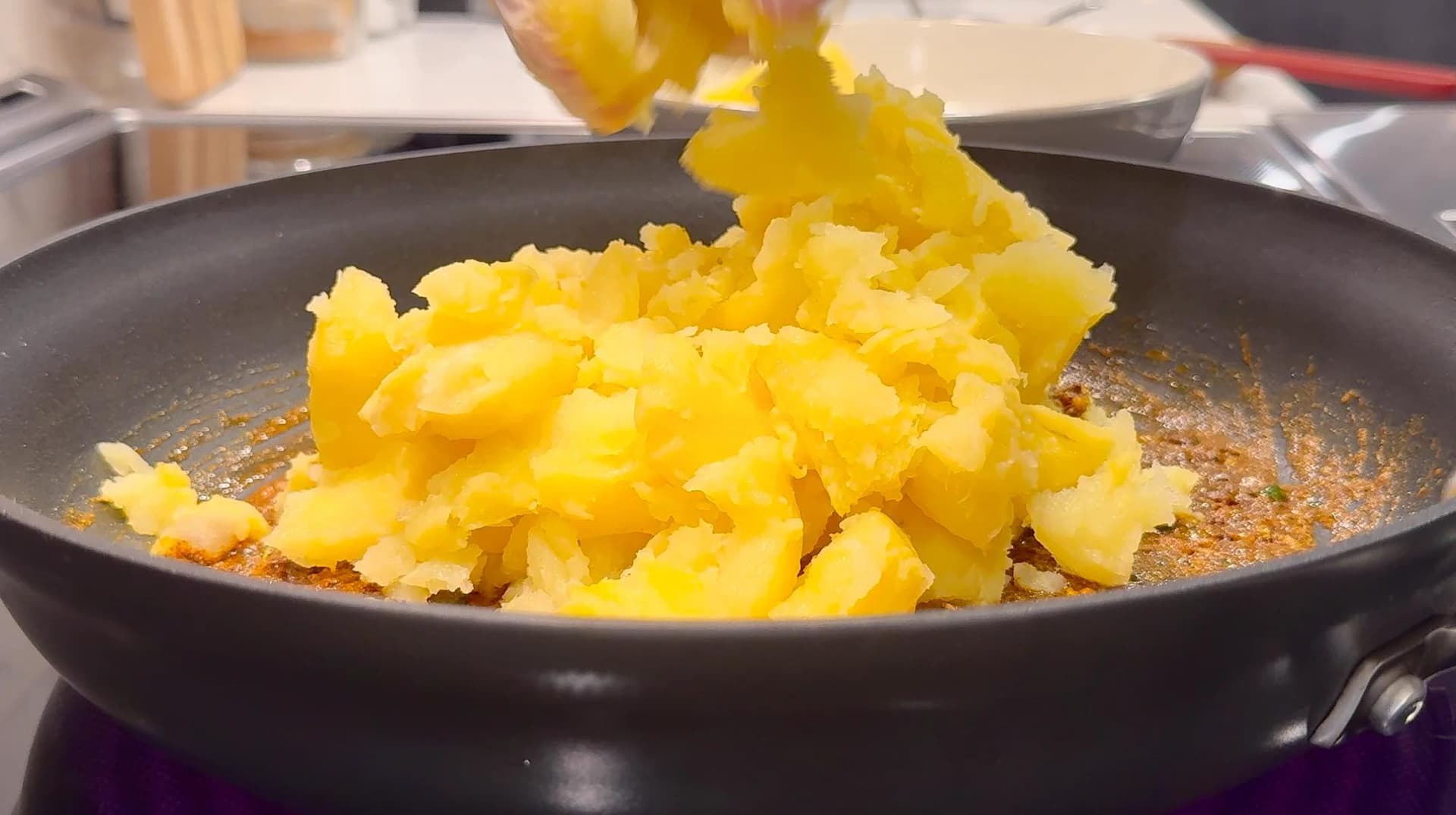 Diced boiled potatoes being stirred in a dark pan with spices during samosa filling preparation.