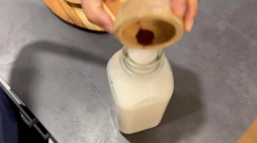 Pouring milk into a bottle with saffron and spices for making Gulabi Doodh Indian pink milk.