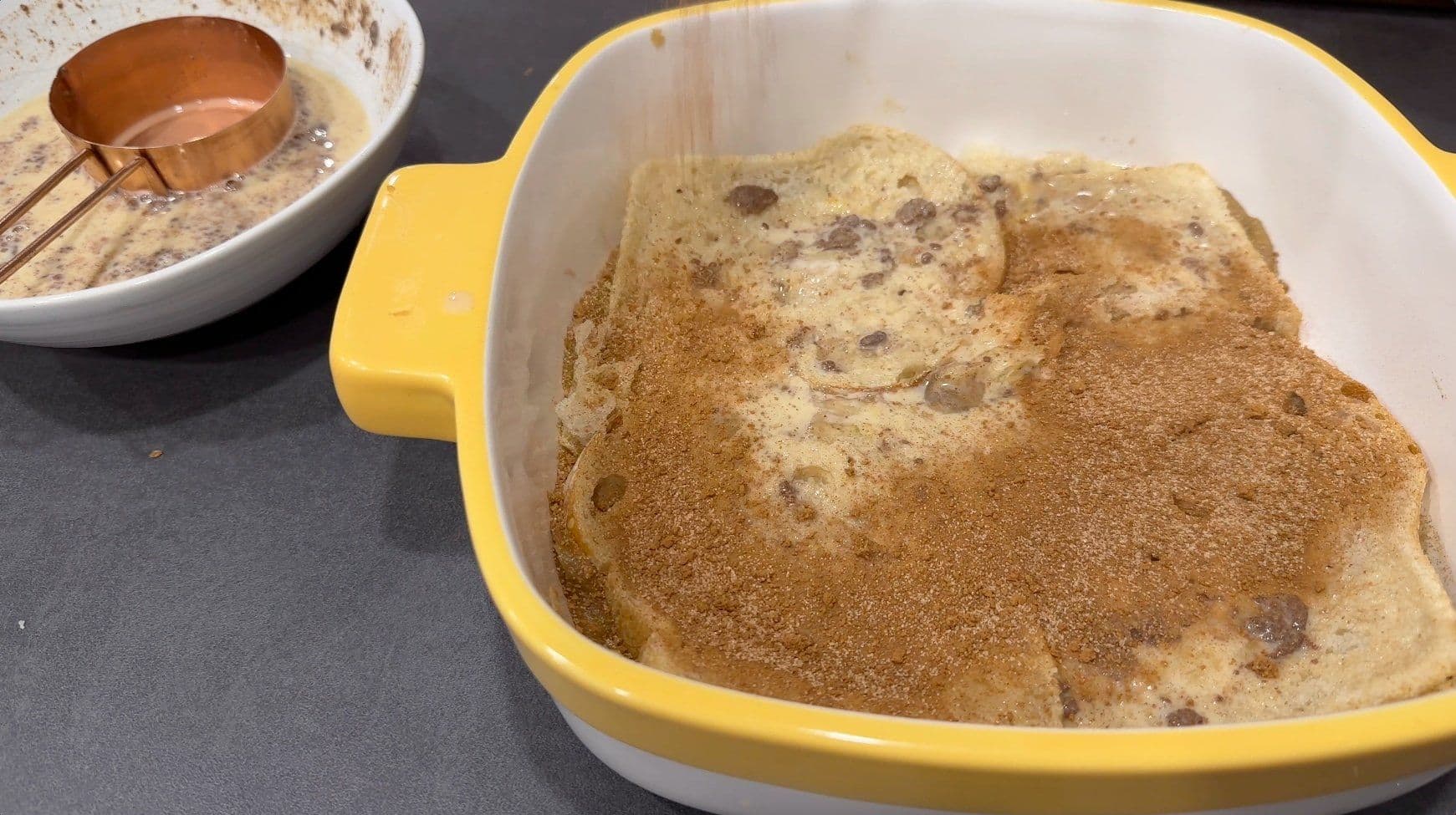 Assembled overnight French toast casserole in yellow baking dish with cinnamon sugar layers and bread pieces soaking in egg mixture.