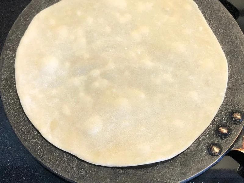 Rolled paratha bread cooking on a hot tawa griddle, showing a light golden surface.