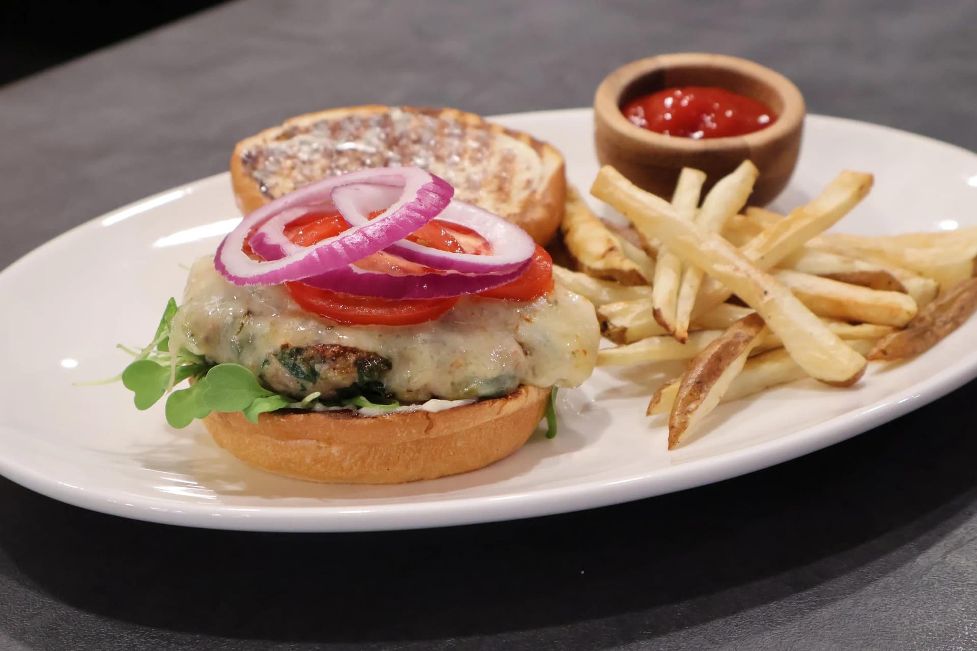 Spinach turkey burger topped with melted cheddar cheese and red onion slices on a toasted bun with arugula, served with a spinach-herb patty.