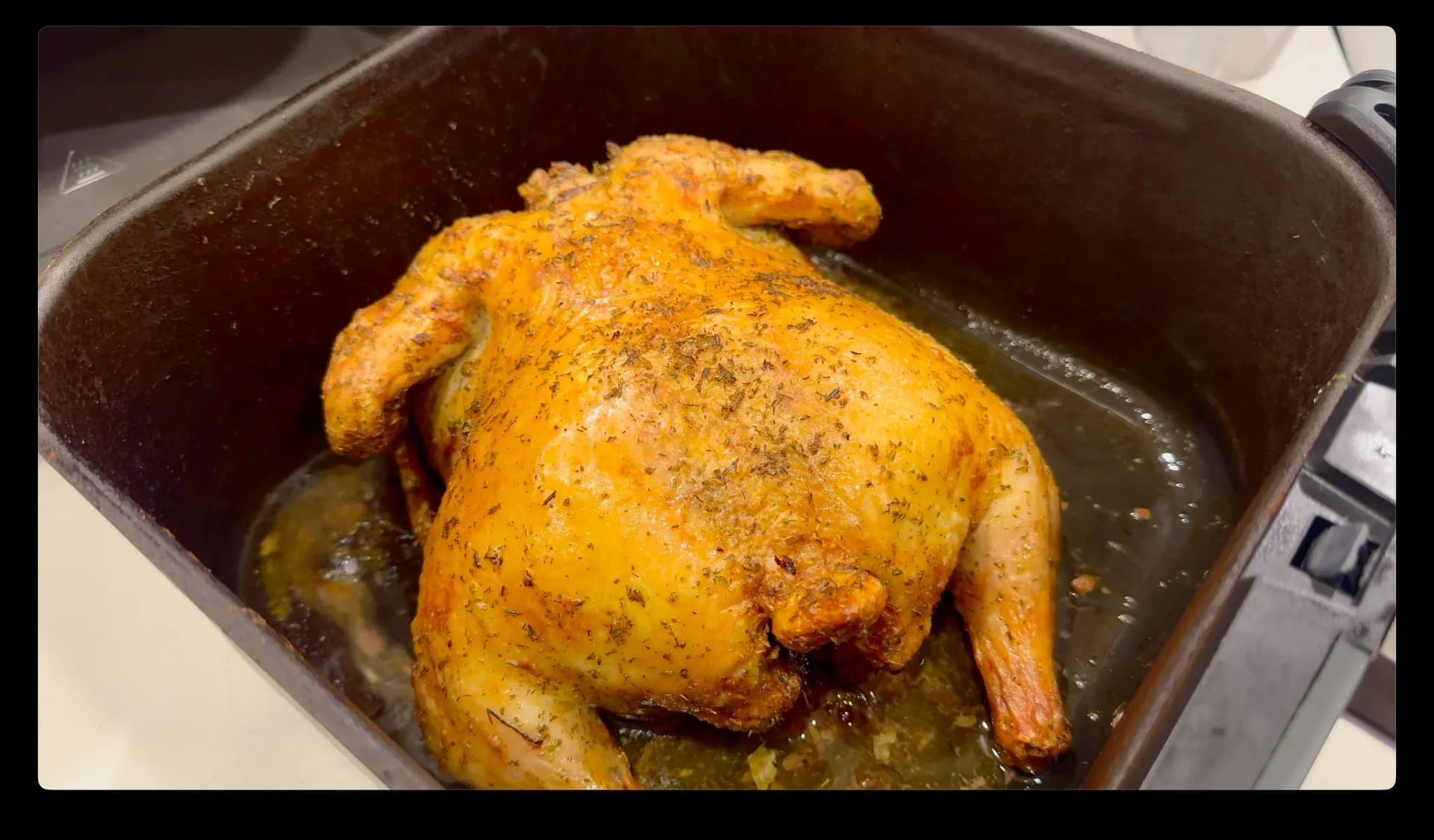Golden-brown whole chicken breast-side down in air fryer basket with seasoning and pan juices.