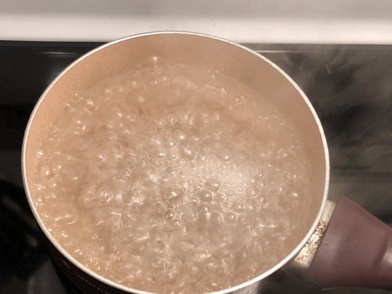Udon noodles cooking in boiling water in a pot on the stove.