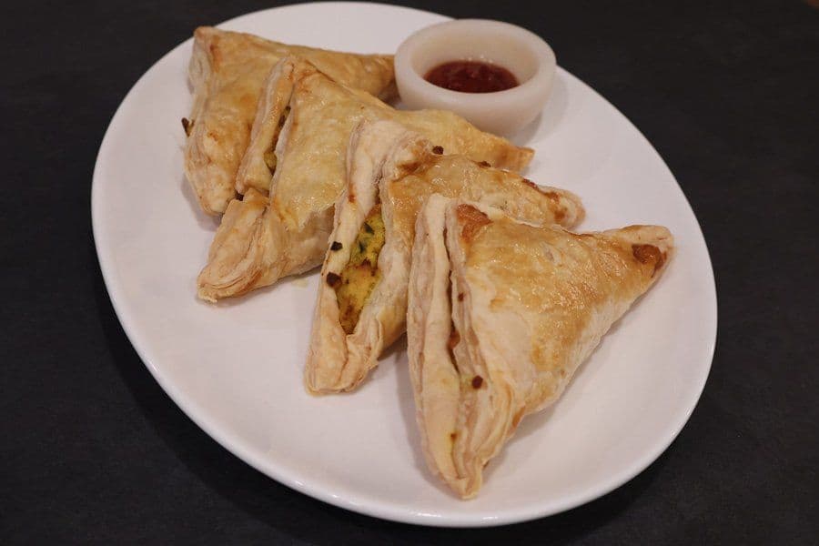 Golden-brown air fryer aloo patties arranged on a white plate with a small bowl of red dipping sauce.