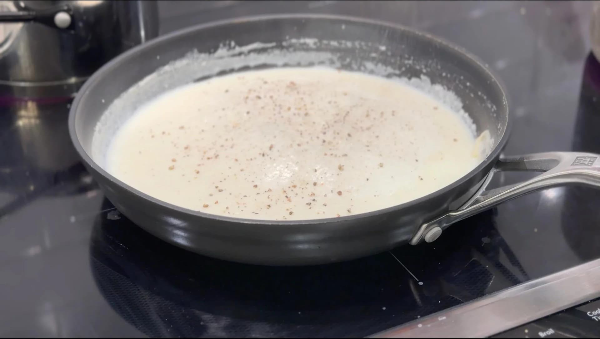 Creamy béchamel sauce simmering in a skillet, sprinkled with nutmeg and black pepper.