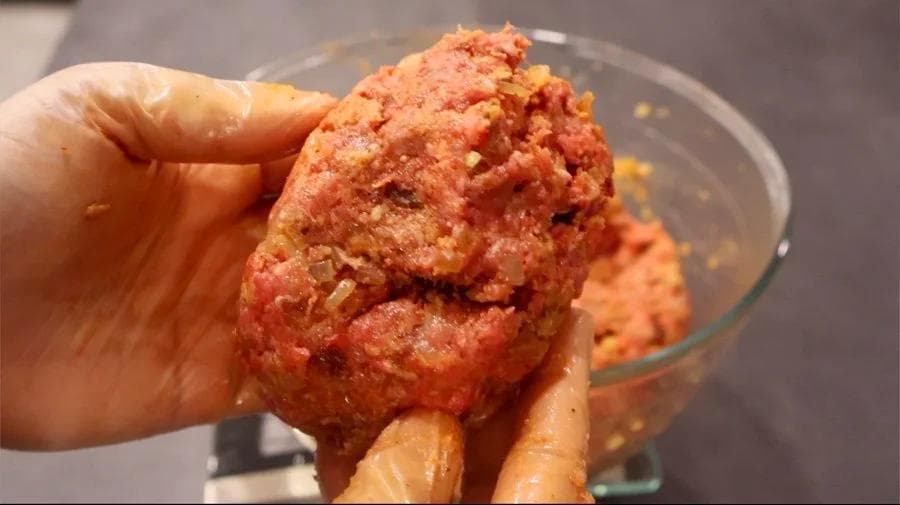 Hand holding a portion of mixed ground beef and chipotle meatloaf mixture over a glass bowl.