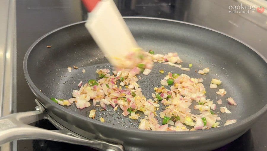 Sautéing diced onions, ham, and green peppers in a dark skillet with a spatula, preparing the vegetable base for aloo patty filling.