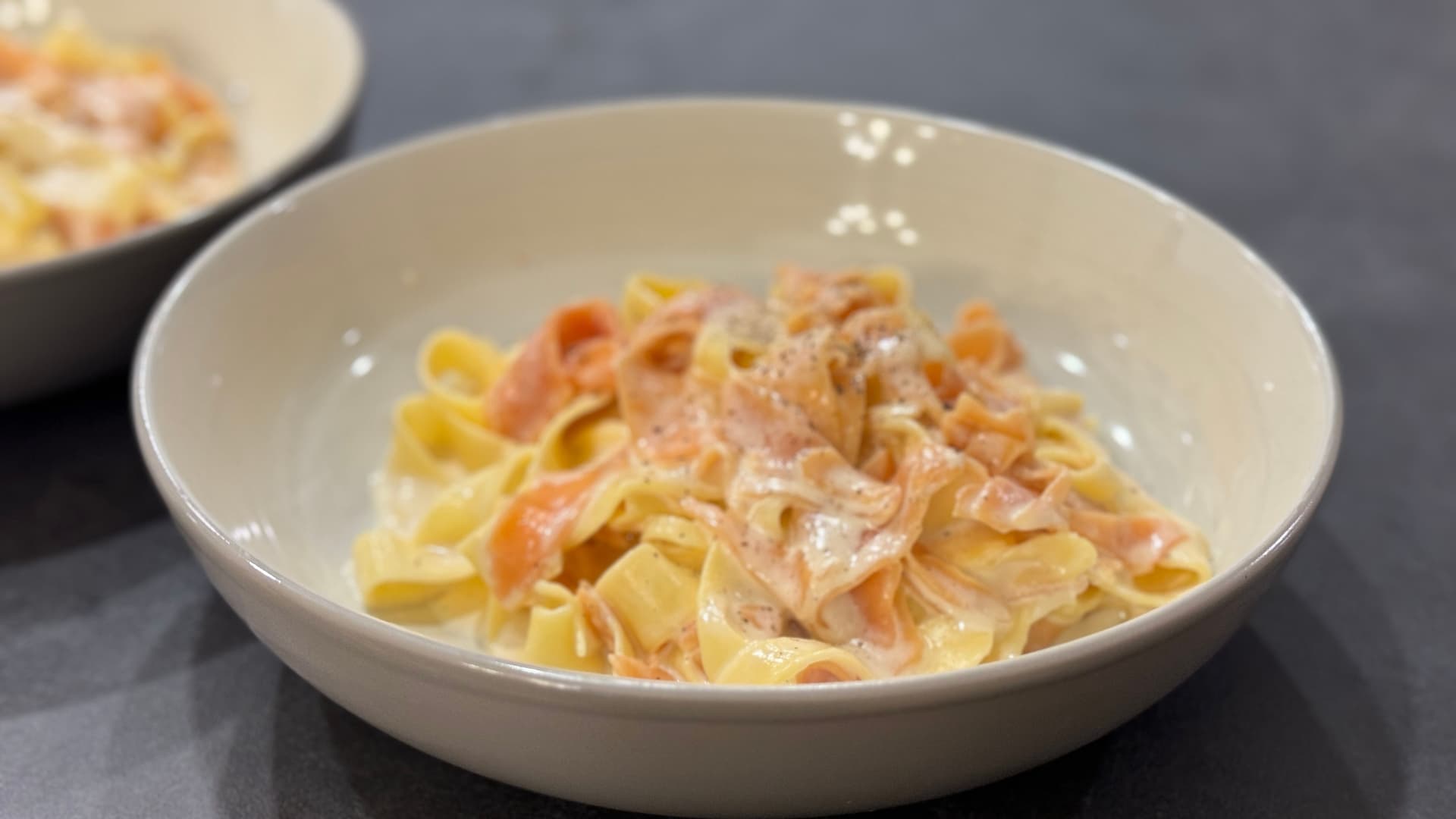 Creamy Alfredo pasta with shredded salmon in a white bowl on a gray surface.