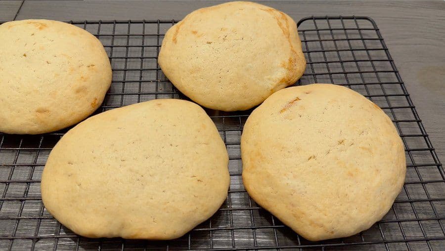 Four baked New York black and white cookies cooling on a wire rack, golden brown with smooth tops.