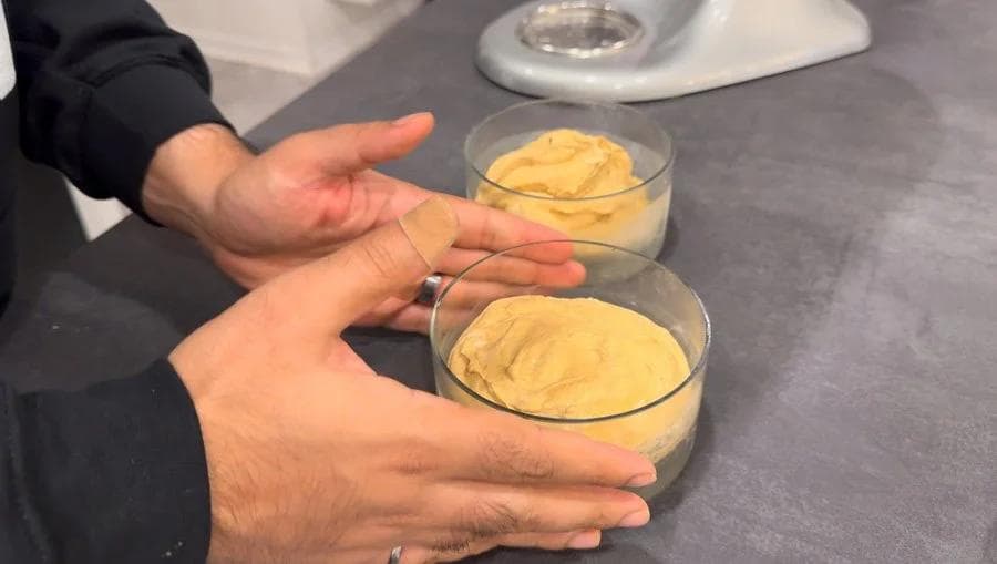 Hands holding two glass bowls filled with creamy yellow pumpkin spice cheesecake mixture before refrigeration.
