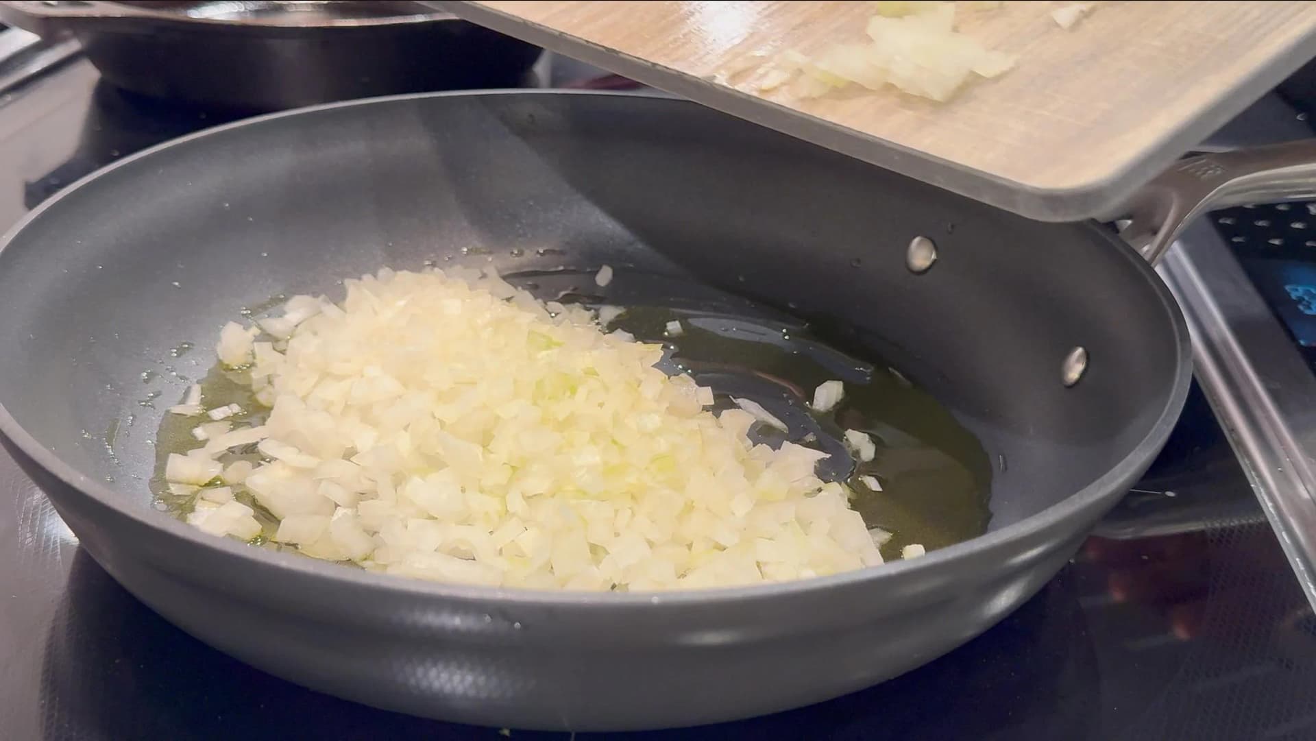 Diced onions sautéing in olive oil in a dark nonstick skillet, soft and translucent after 8 minutes of cooking.