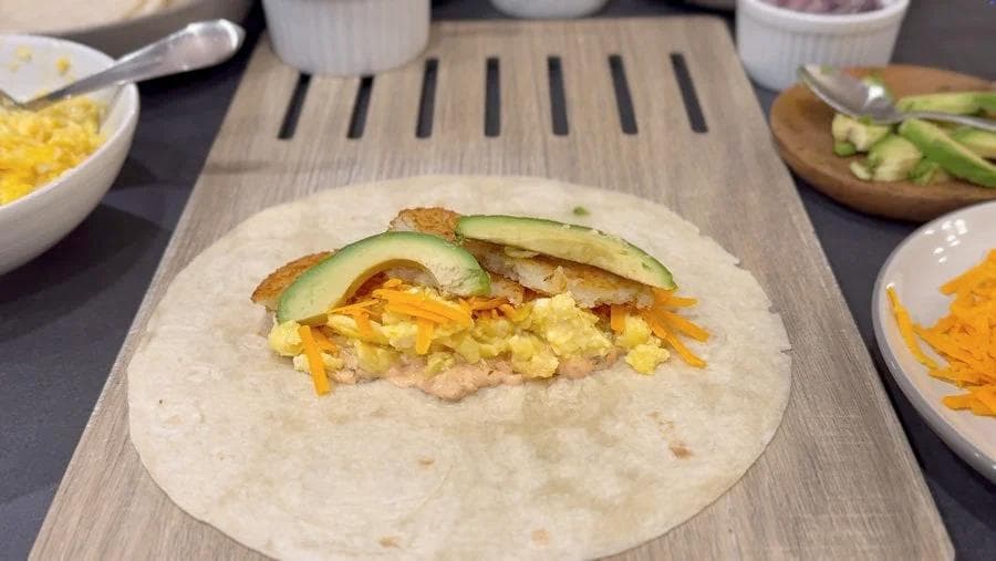 Breakfast burrito filled with scrambled eggs, shredded cheese, and sliced avocado and cucumber on a flour tortilla.