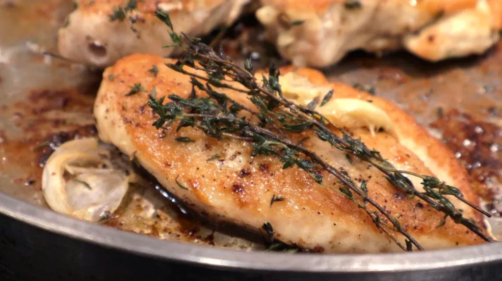 Golden-brown pan-fried chicken breast garnished with fresh thyme sprigs in a skillet with garlic cloves.