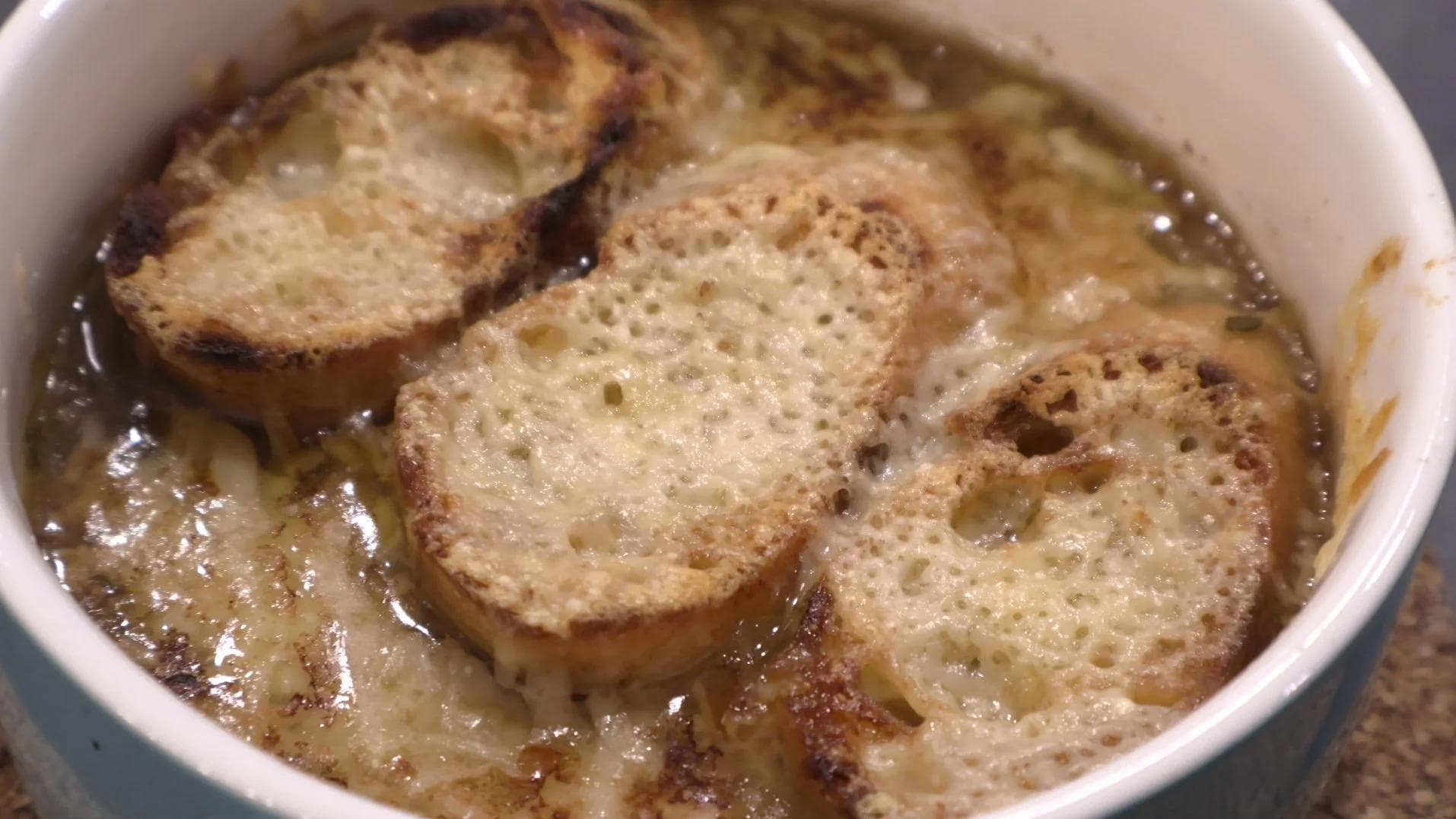 French onion soup with melted cheese and toasted bread slices in white bowl