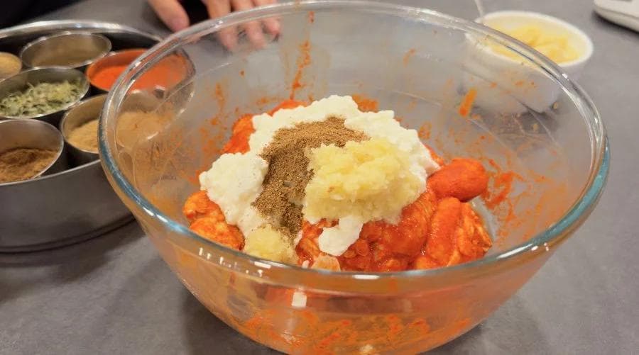 Glass bowl with shredded tandoori chicken, yogurt, ginger-garlic paste, and spices being mixed together for marinating.